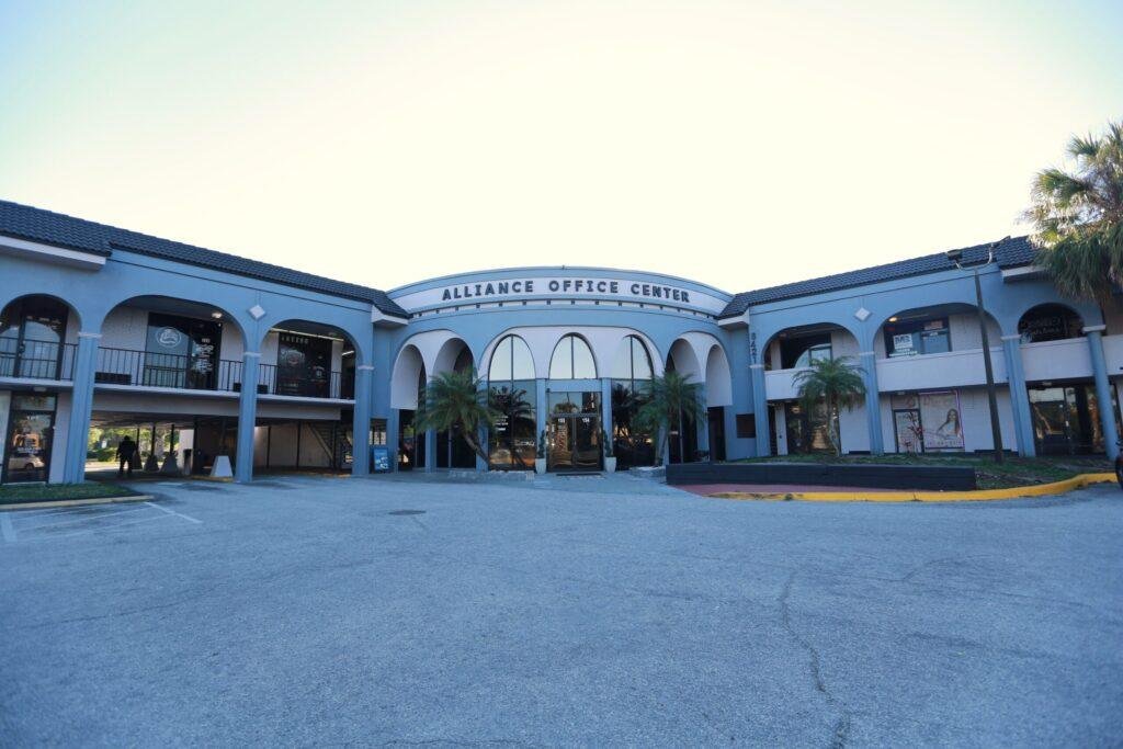 Alliance Office Center commercial building exterior painted in light blue with white trim, featuring Spanish-style arched architecture and palm trees in Orlando, Florida