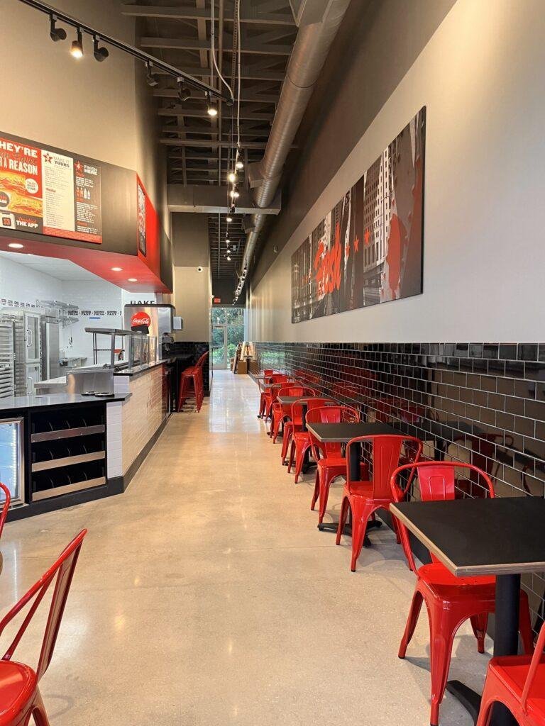Modern Jimmy Johns restaurant interior with bold red seating, industrial design, track lighting, and sleek black tile counter by MJ Renovation Group